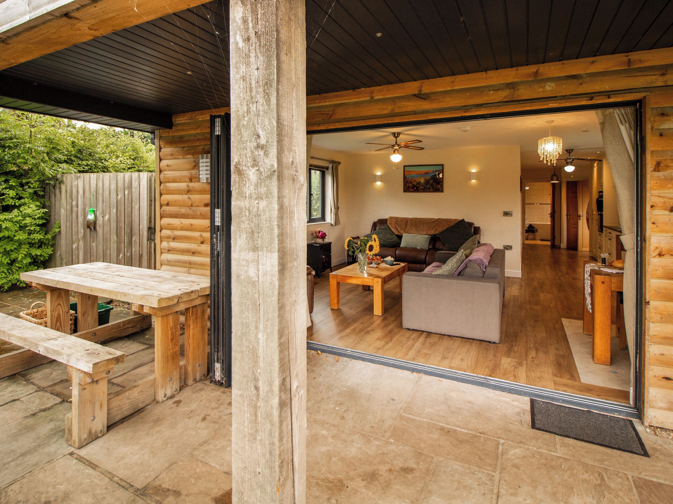 Eine Holzhütte mit einer Terrasse, einem Wohnzimmer mit Sofa und Couchtisch sowie einer Essecke mit einer Bank.