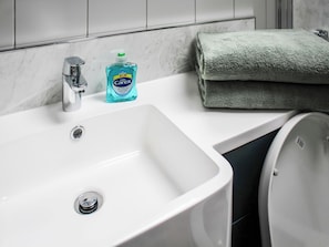 Ein Badezimmer mit einem weißen Waschbecken, einem Chromarmaturen und einer Flasche Carex Handseife.