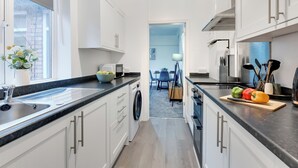 Moderni keittiö, jossa on valkoiset kaapit, musta työtaso ja näkymä ruokailutilaan.