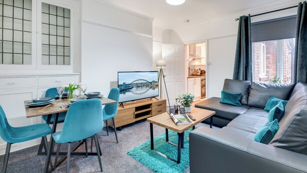 Moderni olohuone, jossa on ruokailutila, sohva, televisio ja avoimen oven kautta näkyvä keittiö.