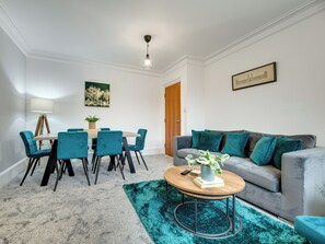 Ein modernes Wohnzimmer mit Essbereich, ausgestattet mit einem grauen Sofa, türkisfarbenen Sesseln, einem Holztisch und einem türkisfarbenen Teppich.