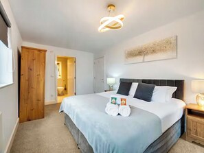 A hotel room with a large bed, a wooden wardrobe, a bathroom visible through an open door, and a modern light fixture. - 2 bedroom accommodation in Newcastle Upon Tyne (Newcastle Upon Tyne)