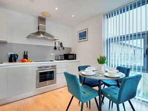 A modern kitchen with a central island, stainless steel appliances, and a dining area with blue chairs and a round table. - 2 bedroom accommodation in Newcastle Upon Tyne (Newcastle Upon Tyne)