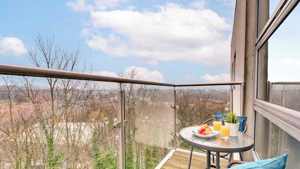 Ein Balkon mit Tisch für zwei Personen, einem Korbsessel und Blick auf die Stadt.