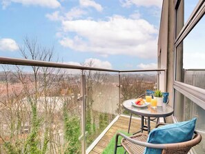 Un balcón con una mesa preparada para dos, una silla de mimbre y vistas a la ciudad.
