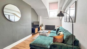 Ein modernes Loft-Apartment mit hohen Decken, einem grünen Sofa, einem runden Spiegel und einem Fernseher auf einer Holzkommode.