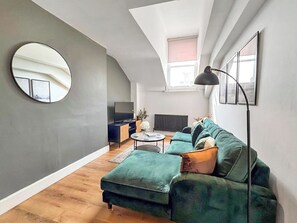 A modern loft apartment with a high ceiling, a green sofa, a round mirror, and a TV on a wooden cabinet. - City Retreat at Queen Street (Newcastle Upon Tyne)