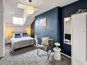 A bedroom with a bed, a chair, a wardrobe, and a small table with flowers. - City Retreat at Queen Street (Newcastle Upon Tyne)