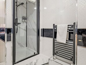 Ein modernes Badezimmer mit einer Glaskabine, einem schwarzen Handtuchhalter und einer Wand mit Marmorfliesen.