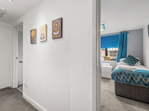 Ein Schlafzimmer mit einem Bett, einem Fenster mit blauen Vorhängen und drei an der Wand befestigten Kunstwerken.