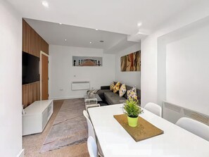 A modern living room with a white sofa, a coffee table with a plant, and a TV mounted on the wall. - 2 bedroom accommodation in Newcastle Upon Tyne (Newcastle Upon Tyne)