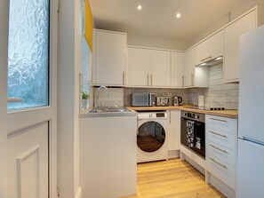 A compact kitchen with white cabinets, a built-in oven, microwave, and a washing machine. - 3 bedroom accommodation in Newcastle Upon Tyne (Newcastle Upon Tyne)