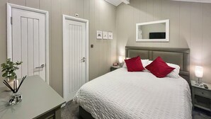 Hotellihuone, jossa on sänky, yöpöydät, työpöytä ja peili seinällä.