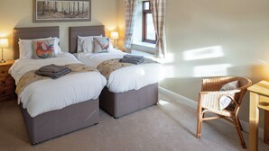 A double bed with a headboard, a bedside table, a lamp, a window with curtains, a chair, and a painting on the wall.