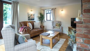 A cozy living room with a brown leather sofa, a plaid armchair, a wooden coffee table, and a brick fireplace.