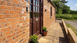A brick building with a brown door and a sign that reads "The Stables." There are two potted plants in front of the door.