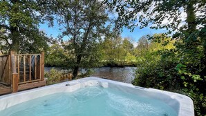 Un jacuzzi en un entorno natural con una terraza de madera y un río al fondo.