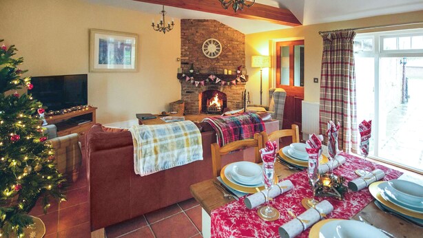 A cozy living room with a fireplace, a Christmas tree, and a dining area set for a meal. - The Coach House - UKC8853 (Blankney Fen)