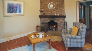 A cozy living room with a brick fireplace, a plaid armchair, a wooden coffee table, and a framed picture on the wall. - The Coach House - UKC8853 (Blankney Fen)