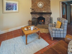 A cozy living room with a brick fireplace, a plaid armchair, a wooden coffee table, and a framed picture on the wall. - The Coach House - UKC8853 (Blankney Fen)