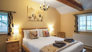 A bedroom with a wooden bed, two bedside tables with lamps, a chandelier, and a window with curtains. - The Coach House - UKC8853 (Blankney Fen)