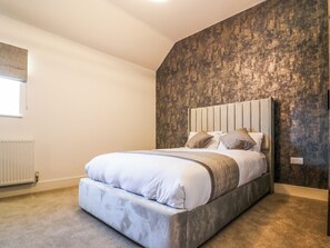 Een slaapkamer met een groot bed, een radiator, een raam en een structuurmuur.