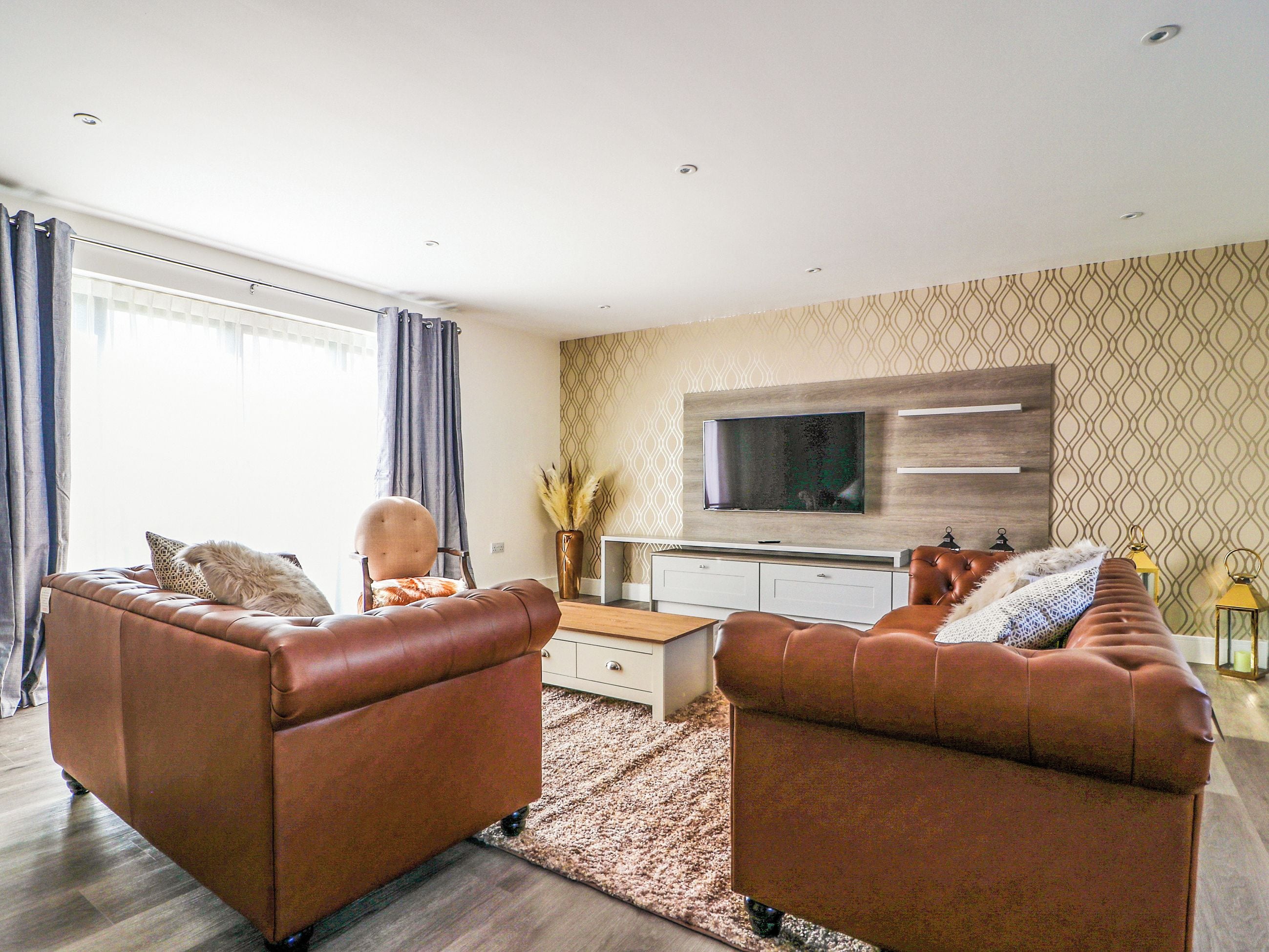 A modern living room with two brown leather sofas, a coffee table, and a flat-screen TV mounted on the wall.