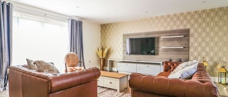 A modern living room with two brown leather sofas, a coffee table, and a flat-screen TV mounted on the wall.