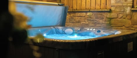A hot tub with a wooden interior and stone walls, surrounded by a wooden deck.