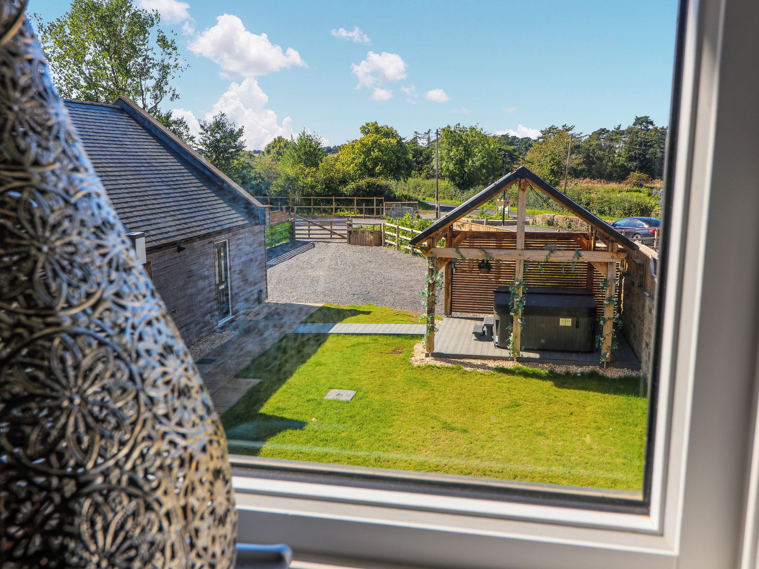 Une vue depuis une fenêtre d’un bâtiment à l’extérieur en pierre, doté d’une terrasse en bois et d’une cour gazonnée.