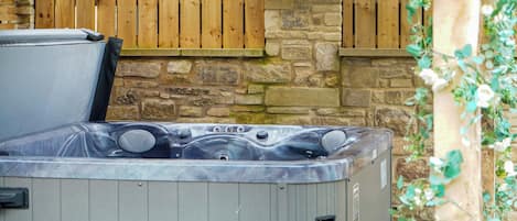 A hot tub with a stone wall and wooden fence in the background.