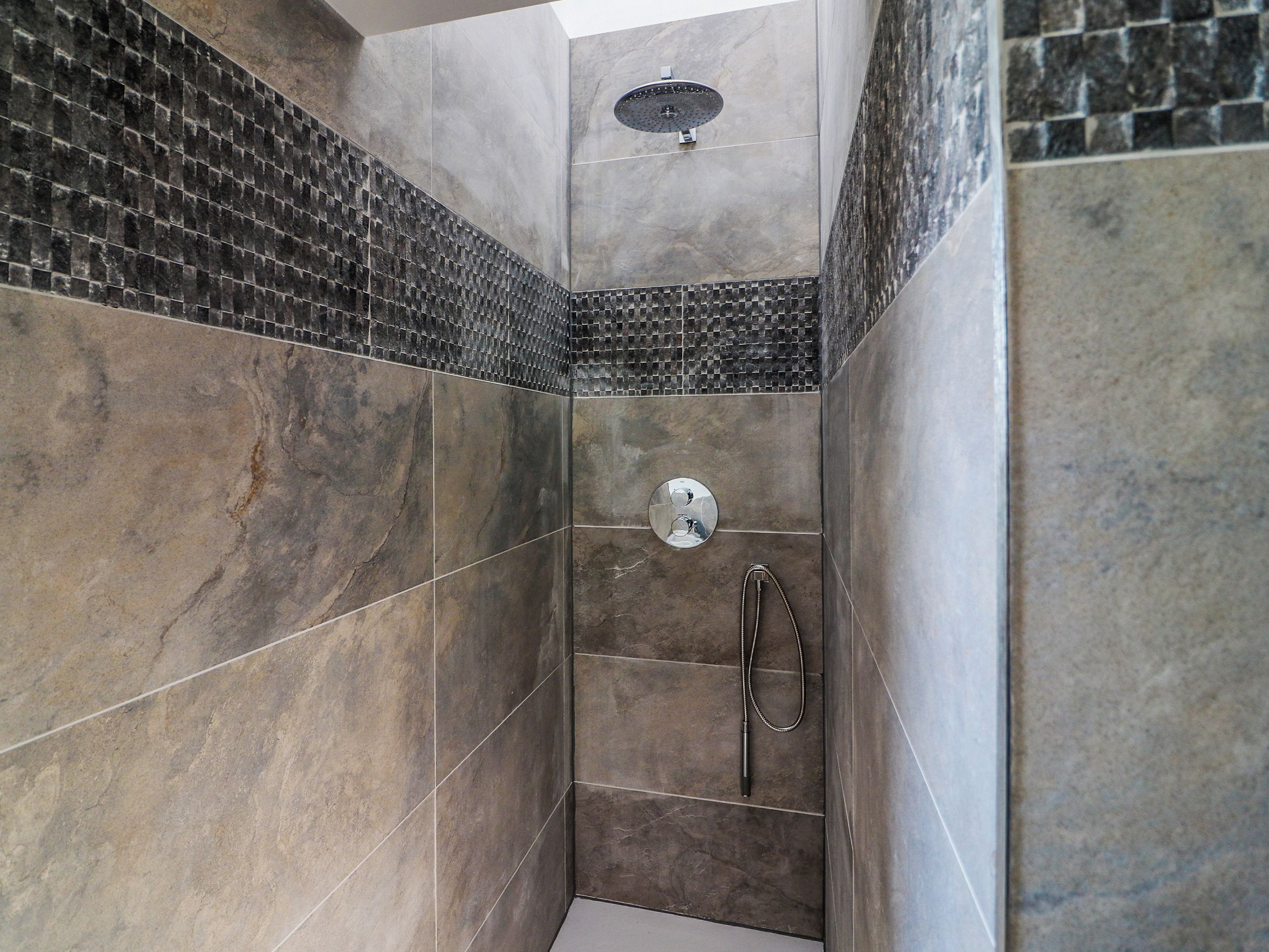 Une douche moderne dotée d’un pommeau de douche à main et d’un robinet mural.