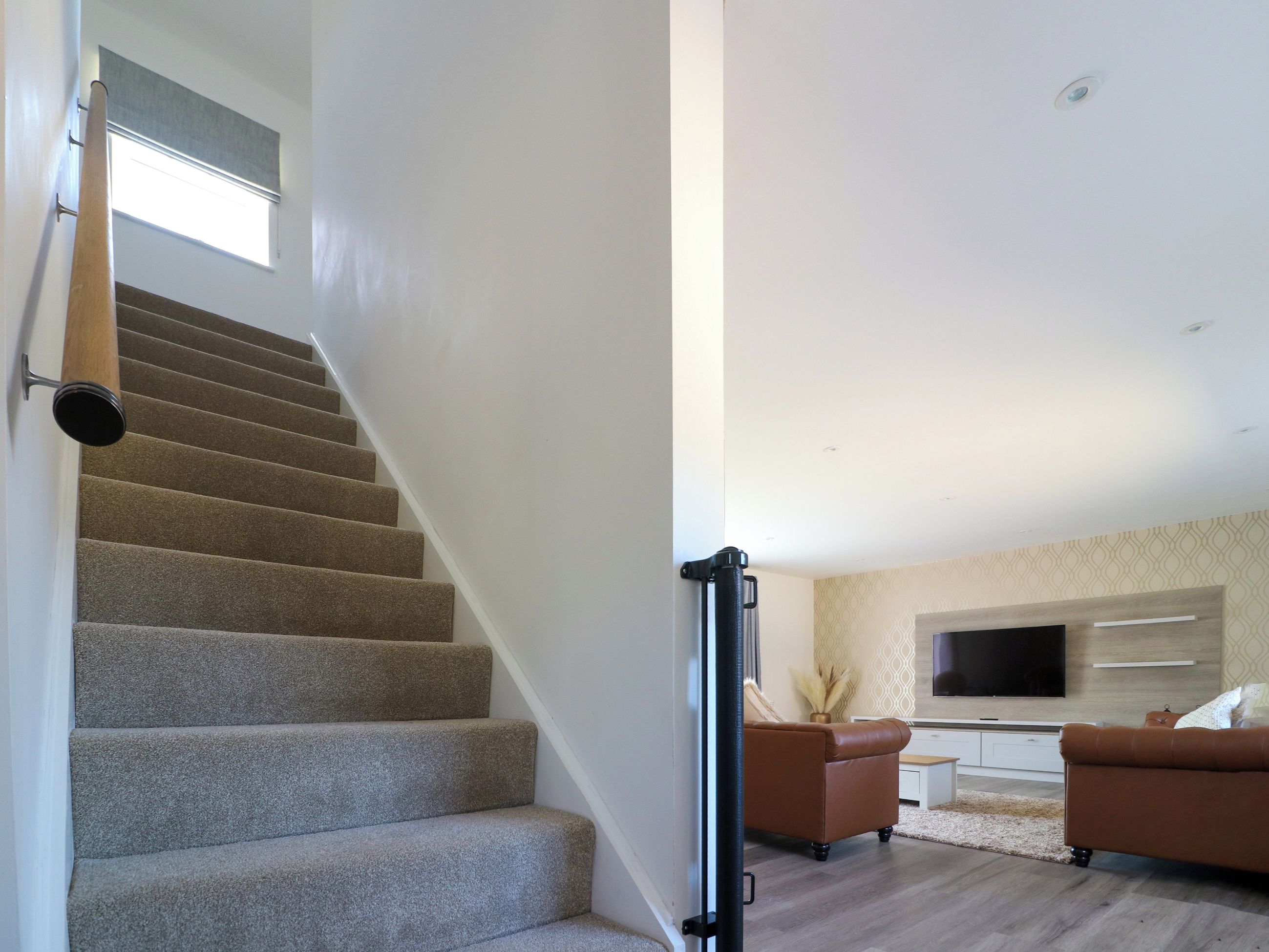 Un escalier mène à un espace de vie comprenant un téléviseur à écran plat, deux canapés et un vase décoratif.