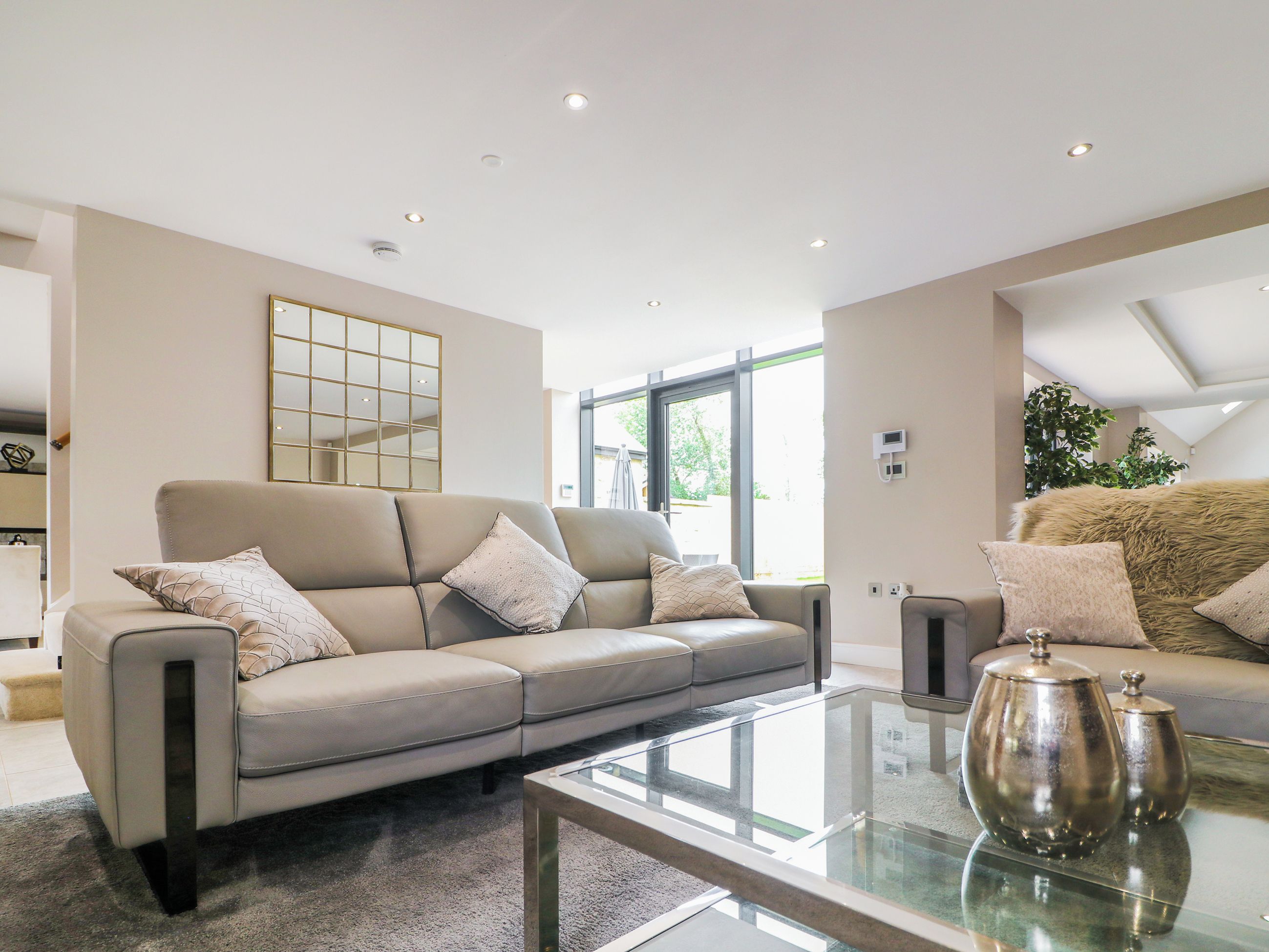 A modern living room with a beige sofa, a glass coffee table, and a large window providing natural light.