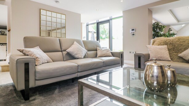 A modern living room with a beige sofa, a glass coffee table, and a large window providing natural light. - 15 Chivits - UKC8971 (Warkworth)