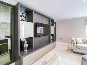 Ein modernes Wohnzimmer mit einem großen Flachbildfernseher an einer Holzwand, einem beigefarbenen Sofa und einem kleinen Beistelltisch.