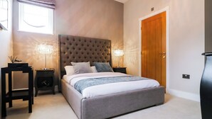A bedroom with a tufted headboard, a large bed, two bedside tables with lamps, a wooden door, and a window with blinds. - 15 Chivits - UKC8971 (Warkworth)