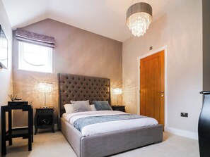 A bedroom with a tufted headboard, a large bed, two bedside tables with lamps, a wooden door, and a window with blinds. - 15 Chivits - UKC8971 (Warkworth)