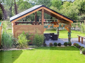 Eine hölzerne Pergola mit geneigtem Dach und einer kleinen Sitzecke mit Kissen.