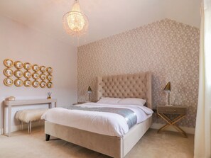Ein Schlafzimmer mit einer gesteppten Kopfteil, einer großen Spiegelwand, einer Chandelüster und einem Nachttisch mit einer Lampe.