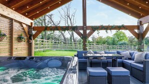A wooden deck with a hot tub, outdoor seating, and a view of the surrounding greenery. - 15 Chivits - UKC8971 (Warkworth)