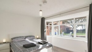 A modern bedroom with a large bed, a bedside table with a lamp, a window with curtains, and a view of the outside. - 6 bedroom accommodation in Murton, near York (Murton, near York)
