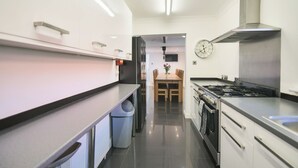A modern kitchen with stainless steel appliances, a dining area with a wooden table and chairs, and a wall-mounted clock. - 6 bedroom accommodation in Murton, near York (Murton, near York)