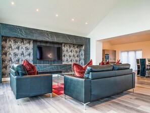 Ein modernes Wohnzimmer mit einem großen Flachbildfernseher an einer strukturierten Wand, zwei dunklen Sofas mit roten Kissen und einem Holzboden.