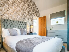 Ein Schlafzimmer mit Wand im Marmor-Design, einem gepolsterten Kopfteil, einer Holztür, einem Schminktisch und einem Fenster mit Blick.