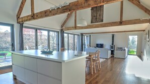 A spacious kitchen with a large island, wooden beams, and a view of the outdoors. - The Cart Shed - UKC8980 (Romsey)