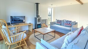A living room with a sofa, a wooden chair, a coffee table, a TV, and a fireplace. - The Cart Shed - UKC8980 (Romsey)