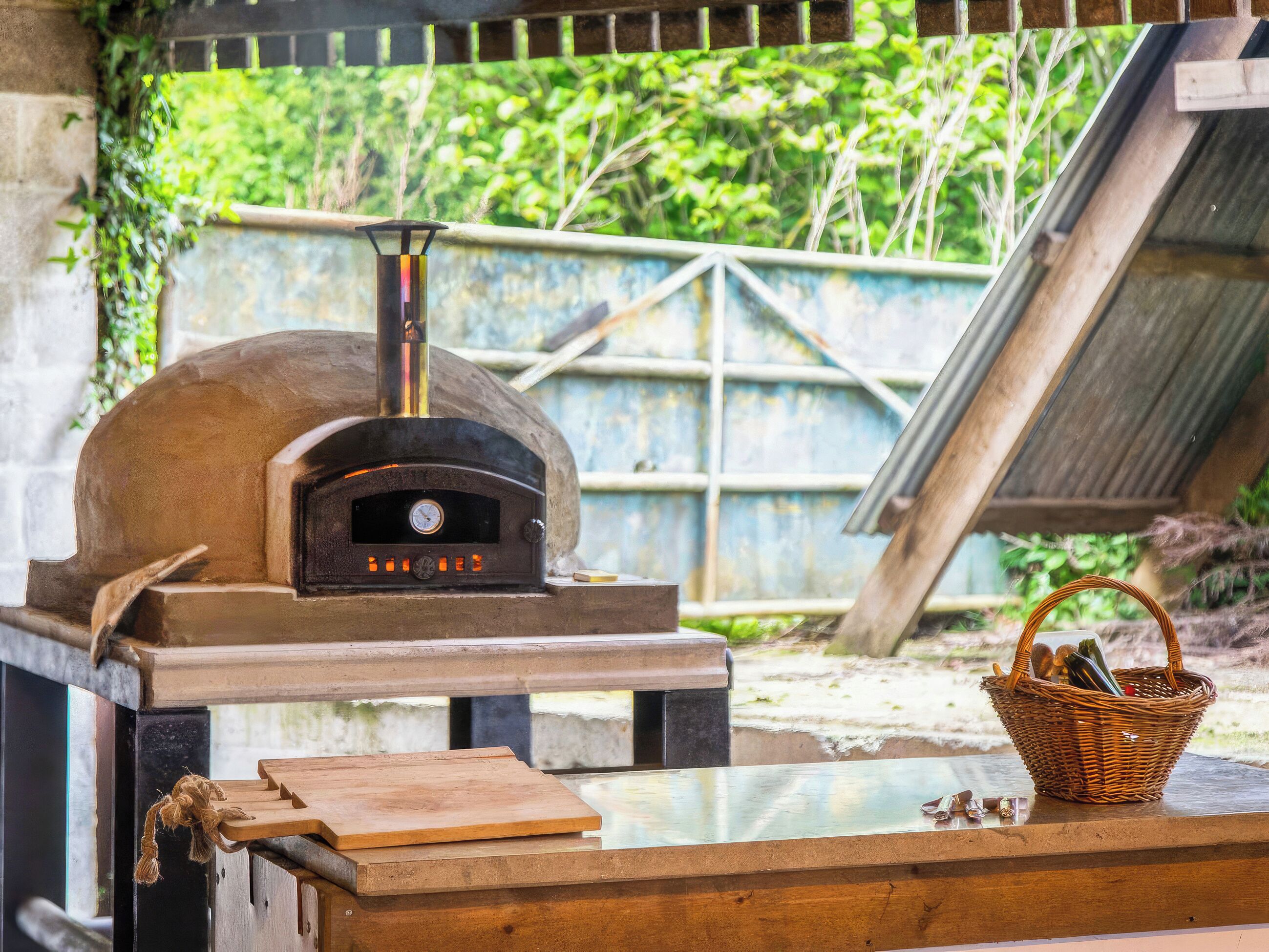 Un four à pizza au bois avec écran numérique, une planche à découper en bois et un panier contenant des ustensiles.