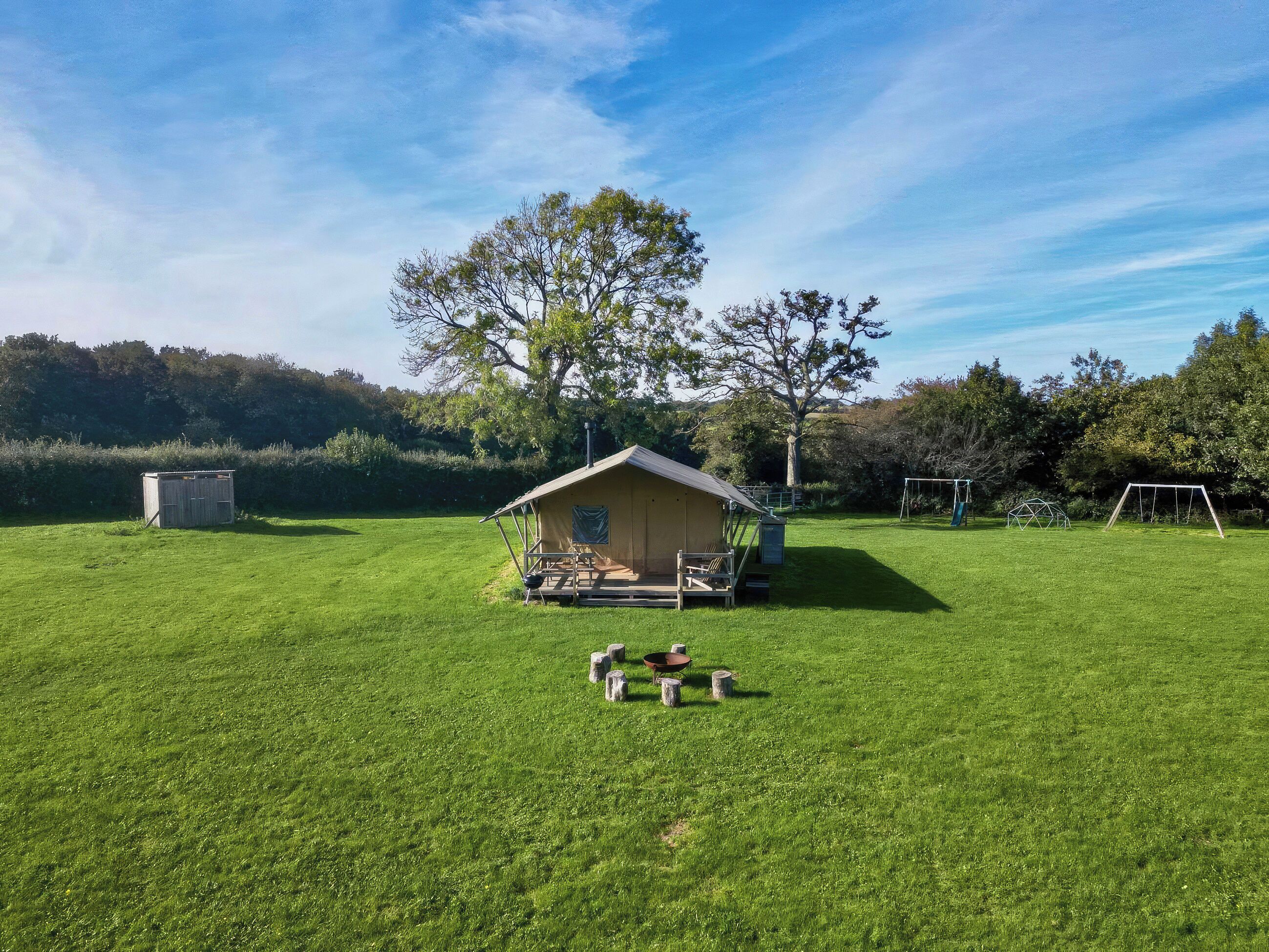 A small, single-story wooden cabin with a porch, surrounded by a well-maintained lawn and trees.