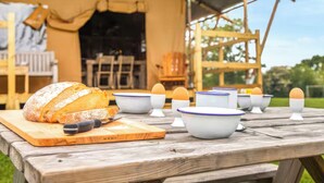 Un'accogliente area pranzo all'aperto con una pagnotta su un tagliere di legno, diverse ciotole con uova e una tenda sullo sfondo.